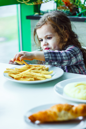 Kid girl in a restaurant eating fast food.の写真素材