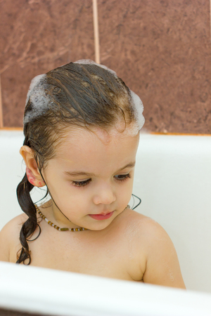 Little kid girl having fun in bathroom with foam on her hairsの写真素材