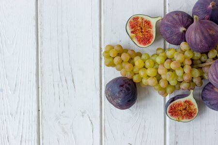 Fresh and ripe fig and grape fruits over white wooden boardの写真素材