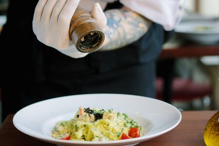Chief hands dressing italian fettuccine pasta with pepper millの写真素材