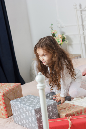 Little kid girl sitting on bed with the boxes of christmas gifts.の写真素材