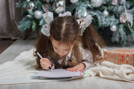 Little kid girl writing letter with wishes to Santa Claus on christmas day.の写真素材