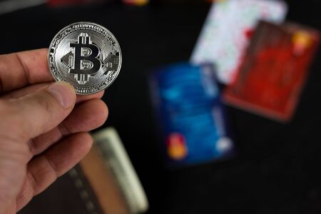 One bitcoin coin in hand against credit cards on background.の写真素材