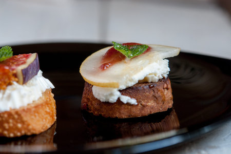 Bruschetta with goat cheese, pear and figs on black plate