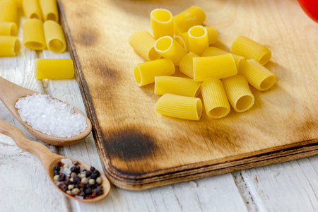 Dry rigatoni pasta on wooden board surrounded by vegetables.の写真素材