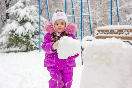 Little kid girl builds snowman on winter day outdoors.の写真素材