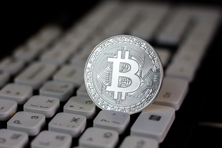 Silver bitcoin coin on white pc keyboard.の写真素材