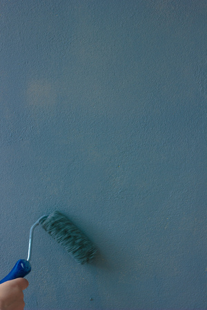 Hand with paint roller over the blue wall.の写真素材