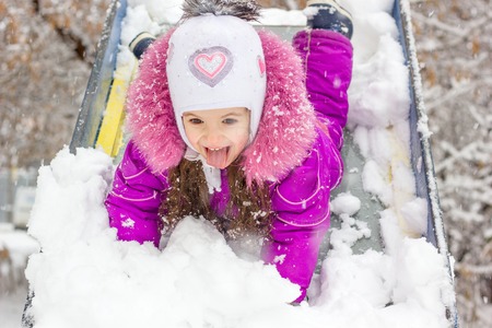 Kid girl on children slide at snowy winter day.の写真素材