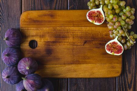 Wooden kitchen board with fig fruits and grapes on it.の写真素材