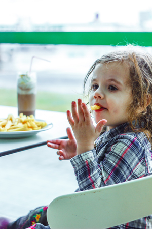 Kid girl in a restaurant eating fast food.の写真素材