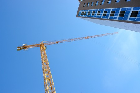 Construction tower crane and new building over blue sky background.の写真素材