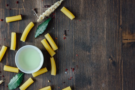 Tortiglioni pasta with bay leaves, olive oil and other ingredients on brown wooden surface.の写真素材
