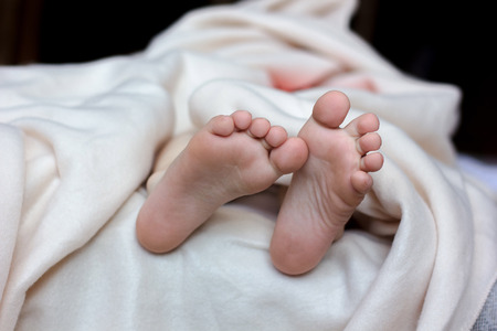 Kid laying in the bed and foot with toes and heels on white blanketの写真素材