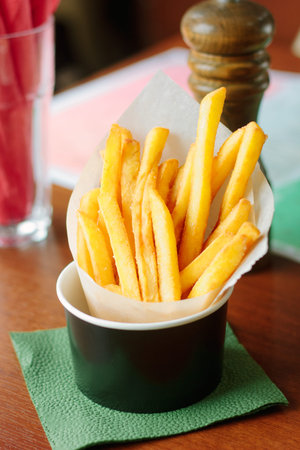 French fries rolled in parchment inside black cup on table, great image for your needs.