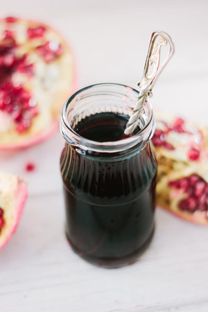 Pomegranate sauce on glass bottle surrounded by pomegranate halves.