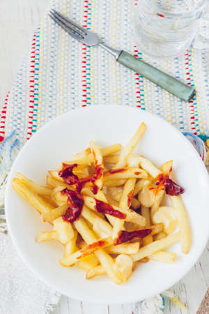 Poutine fries with tomato sauce and cheese on white table.の写真素材