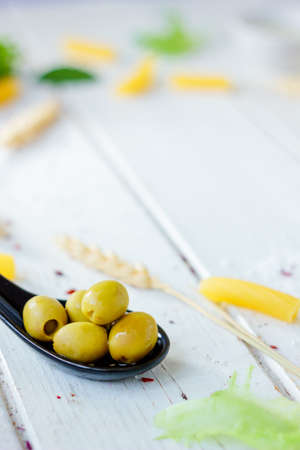 Green olives on black spoon over white wooden background.の写真素材