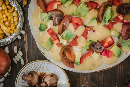 Vegetarian home made pizza with mushrooms and vegetables over wooden table, surrounded by ingredientsの写真素材