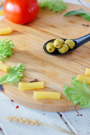 Green olives on black spoon over brown kitchen board.の写真素材
