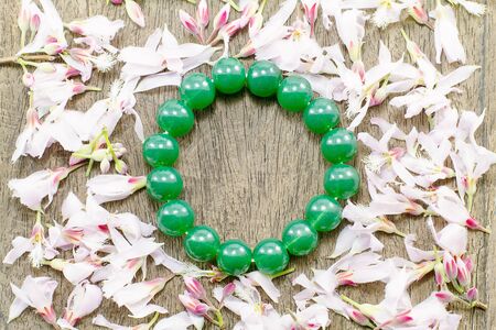 Green round stone  bracelet surrounded by pink flowers on vintage grunge wooden backgroundの写真素材