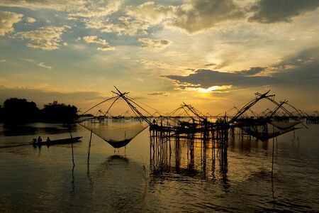 Sunrise at the fisherman village with silhouette of wooden fishing net and long tail wooden boat , Pakpra, Pattalung, Thailandの写真素材