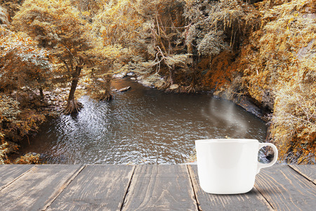 Hot coffee with smoke on vintage wooden table top on blurred waterfall backgroundの写真素材