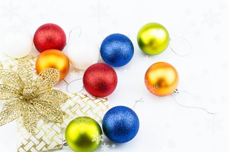 Colorful christmas balls with golden flower ribbon and snowflakes on white backgroundの写真素材