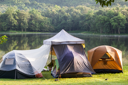 Camping tent on green grass beside lake with forest background  during sunrise, Thailandの写真素材