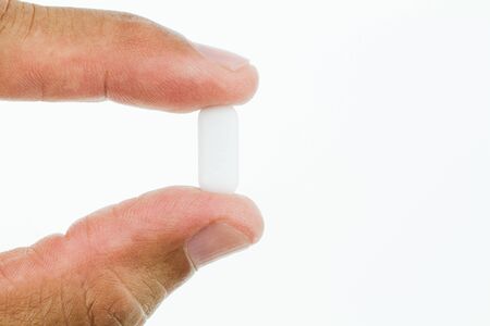 Macro of man's fingers holding white pill isolated on white background, medical conceptの写真素材