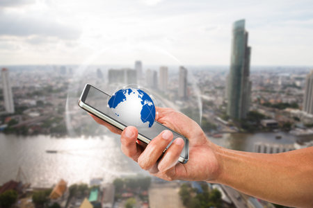 Man's hand holding mobile phone with globe on blurred city background, technology communication...