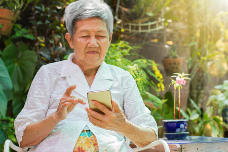 Asian elderly women sitting in garden holding smartphoneの写真素材