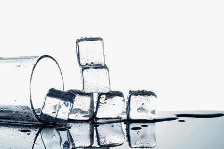 Ice cubes and empty glass on glossy table on white background