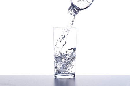 Pouring drinking water from bottle into glass on white background