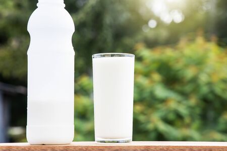 Bottle and glass of fresh milk on wooden table on blurred green nature backgroundの写真素材