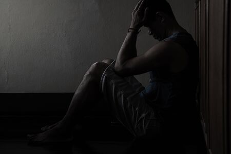 Desperate hopeless man with hands holding head sitting in dark corner の写真素材
