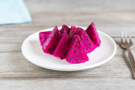 Sliced pink dragon fruit on white ceramic plate on vintage wooden table, selective focusの写真素材