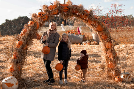 mother with children stands with pumpkins in their hands under an arch with pumpkinsの写真素材