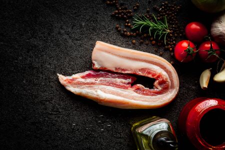 raw pork belly with garlics, tomatoes, rosemarry,Olive oil, pepper, bbq sauce and on stone black background, dark picture style.の写真素材