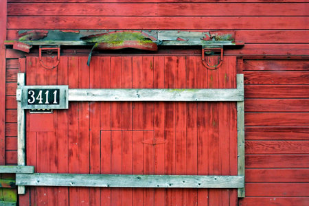 Weathered sliding barn door with addresss, hanging on old red barn.の写真素材