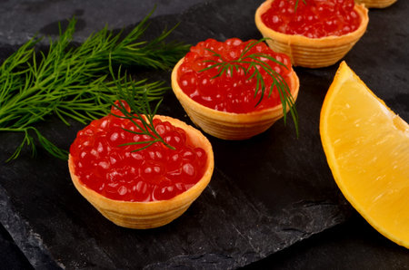 Tartlets with red salmon caviar on black stone plate, decorated with dill and a slice of lemon, close - up. Seafood appetizerの写真素材