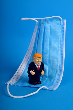 Riga, Latvia - January 07, 2021: Small Donald Trump figure standing on a blue face protection mask, cartoon, parody of Donald Trump, Covid - 19 concept, blue backgroundのeditorial素材