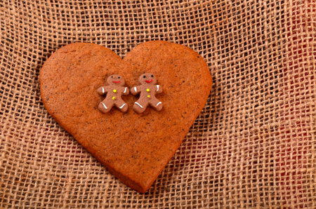 Gingerbread men on gingerbread hearts, coarse cloth background. Christmas card concept