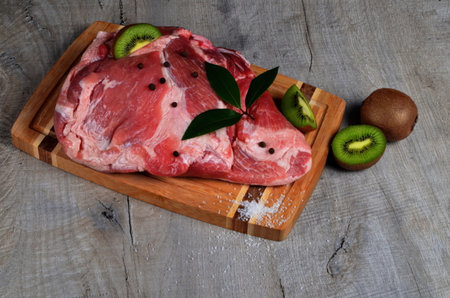 Raw pork meat, pork with kiwi fruit on a wooden cutting board. Kiwi fruit makes the meat softの写真素材