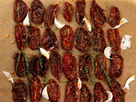 Sun dried tomatoes, dried tomato halves with thyme, garlic on olive oil on baked paper, top viewの写真素材