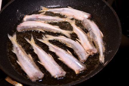 Crispy breaded European smelt fish (Osmerus eperlanus) in a black kitchen pan. Small fish fry in a...