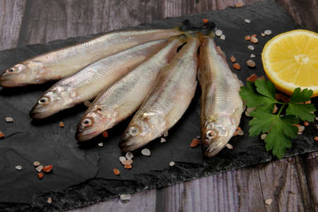 Fresh smelt fish on a black stone plate, Smelt fishes (European smelt) with lemon and green parsley, Group of fresh smelt fishの写真素材