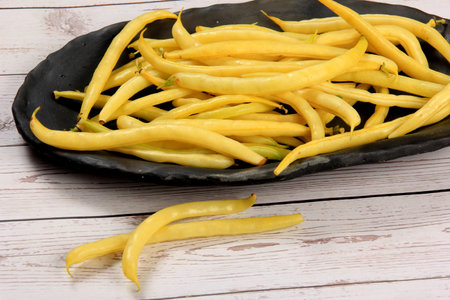 Yellow wax string beans on black clay plate, white wooden board background. Organic vegetables from...