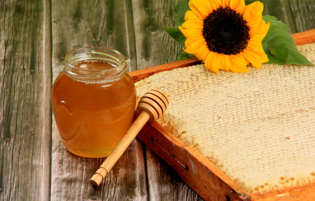 Honeycomb in a wooden frame decorated with sunflower and glass jar of honey on a wooden background....