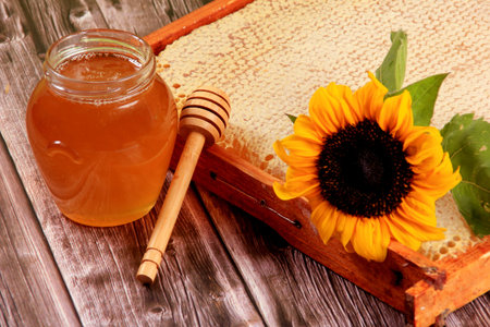 Honeycomb in a wooden frame decorated with sunflower and glass jar of honey on a wooden background....